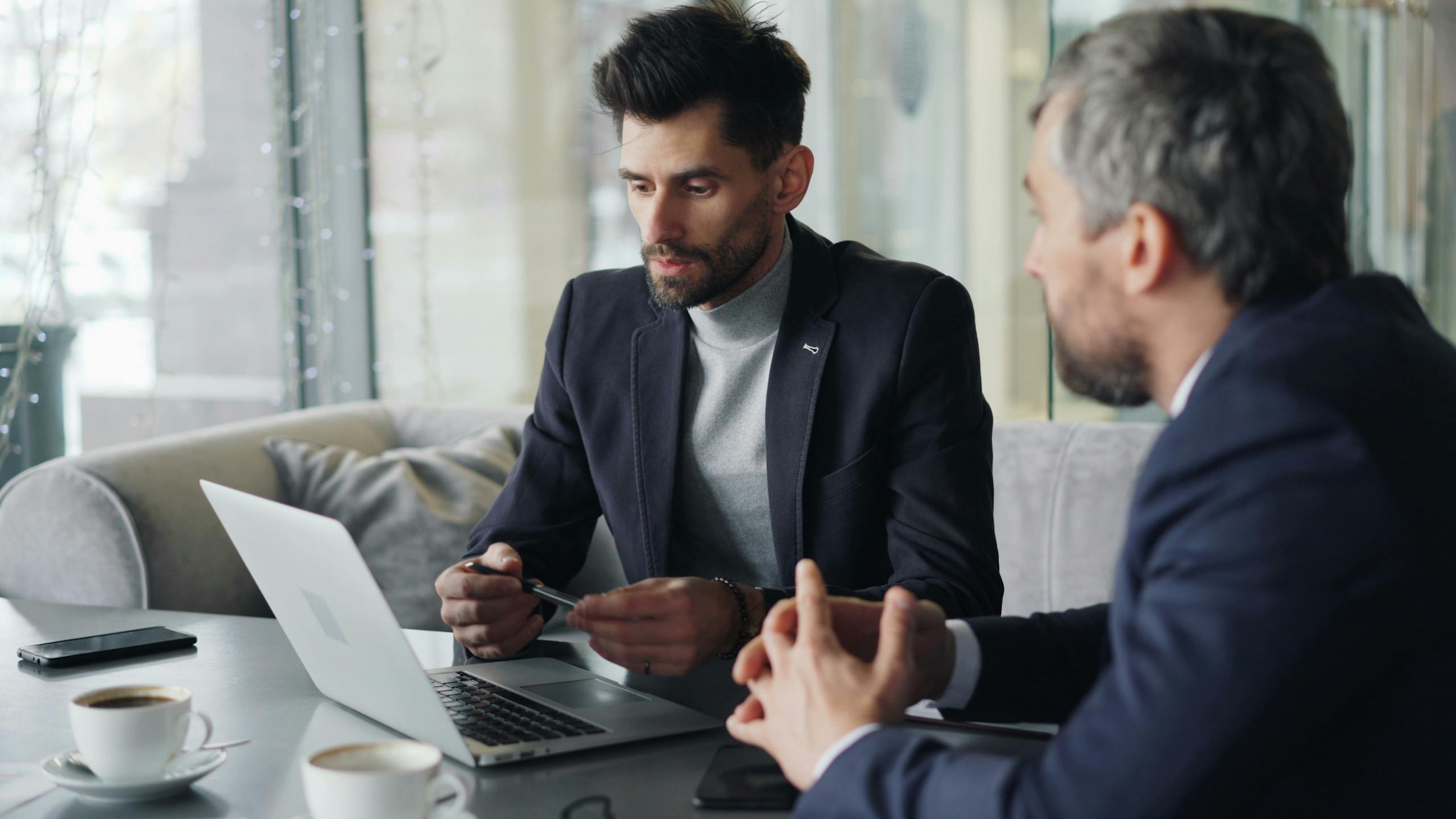 Two businessmen engaged in a meeting in a cozy café, discussing on a laptop.